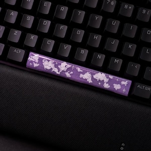Könnte beinhalten: Benutzerdefinierte Leertaste für die Tastatur mit lila Basis und Wolkenmuster. Die Leertaste liegt auf einer schwarzen Tastatur und einer schwarzen Oberfläche.