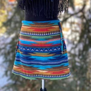 May include: A colorful, geometric patterned fleece skirt with a turquoise, brown, red, and green design. The skirt has a tie closure and is on a mannequin.
