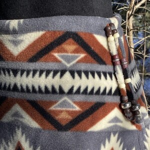May include: A grey, brown and white patterned fleece skirt with a beaded trim. The beads are brown, white and purple.