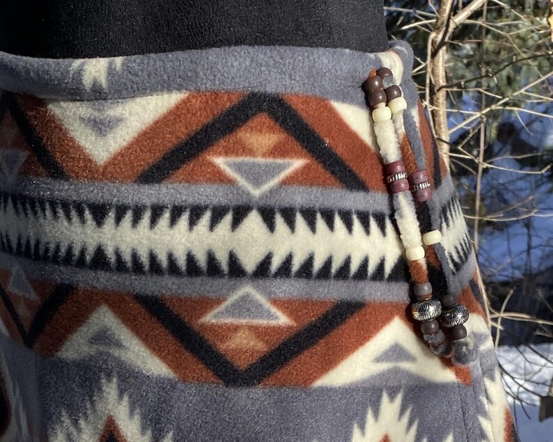May include: A grey, brown and white patterned fleece skirt with a beaded trim. The beads are brown, white and purple.