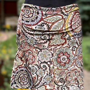 Op de afbeelding: Een witte rok met een paisley print in tinten rood, groen en bruin. De rok is gemaakt van een zachte, rekbare stof en heeft een geplooide tailleband.