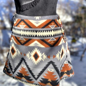 May include: A grey fleece skirt with a geometric pattern in shades of brown, black, and white. The skirt has a wrap-around style and a beaded accent on the side.