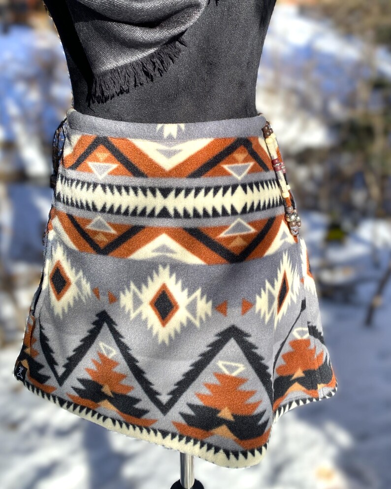 May include: A grey fleece skirt with a geometric pattern in shades of brown, black, and white. The skirt has a wrap-around style and a beaded accent on the side.