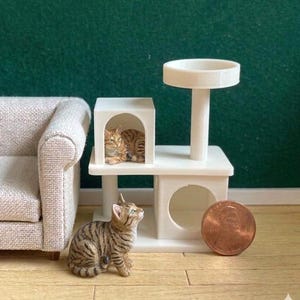 May include: Miniature cat furniture set with a small tabby cat figurine. The set includes a white cat tree with a perch, a hideaway, and a round opening. A penny is placed next to the cat tree for scale.