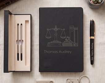 May include: A black notebook with a scale of justice and gavel engraving, the name Thomas Audrey, a black pen with gold accents, a rectangular USB drive, and a square keychain, all featuring the name Thomas Audrey and legal motifs.