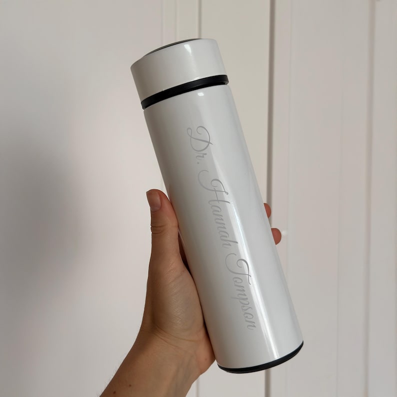 May include: White stainless steel water bottle with a black lid and the name "Dr. Hannah Thompson" engraved on the side.