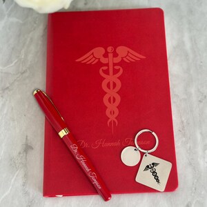 May include: Red leather journal with a gold pen and a keychain with a medical symbol. The journal is personalized with the text "Dr. Hannah Thompson".