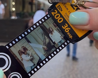 Op de afbeelding: Een gepersonaliseerde foto sleutelhanger met een filmstrip met drie afbeeldingen. De sleutelhanger heeft een zwarte filmstrip, een zilveren ketting en een gele Kodak filmrol met de tekst "200 36exp."