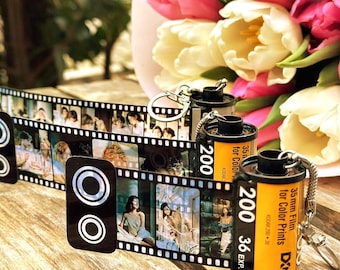 Op de afbeelding: Een 35mm filmrolletje sleutelhanger met een uitrolbare strook fotofilm. Het geel-zwarte rolletje is gelabeld met 200 36 EXP. De bevestigde filmstrook toont een reeks kleurenfoto's met verschillende mensen erop afgebeeld.