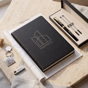 May include: A black notebook with a silver geometric logo and the text Martin K. on the cover, a black pen with gold accents in a gift box, a silver square keychain with the same logo, and a silver rectangular USB drive labeled Martin K.