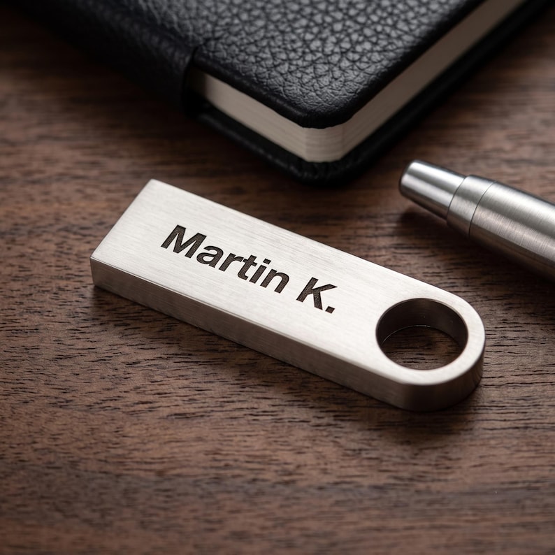 May include: A rectangular silver-toned metal USB flash drive with a brushed finish and a circular cutout at one end. The name Martin K. is engraved in a dark, sans-serif font on the top surface of the drive, which is positioned horizontally.