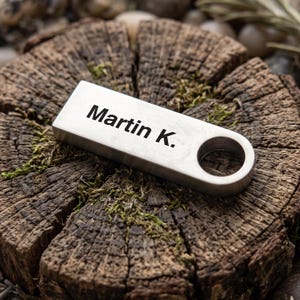 May include: A rectangular silver-toned metal keychain tag with a brushed finish and a circular hole on one end. The surface is engraved with the black text Martin K. in a clean sans-serif font, positioned horizontally across the center of the piece.