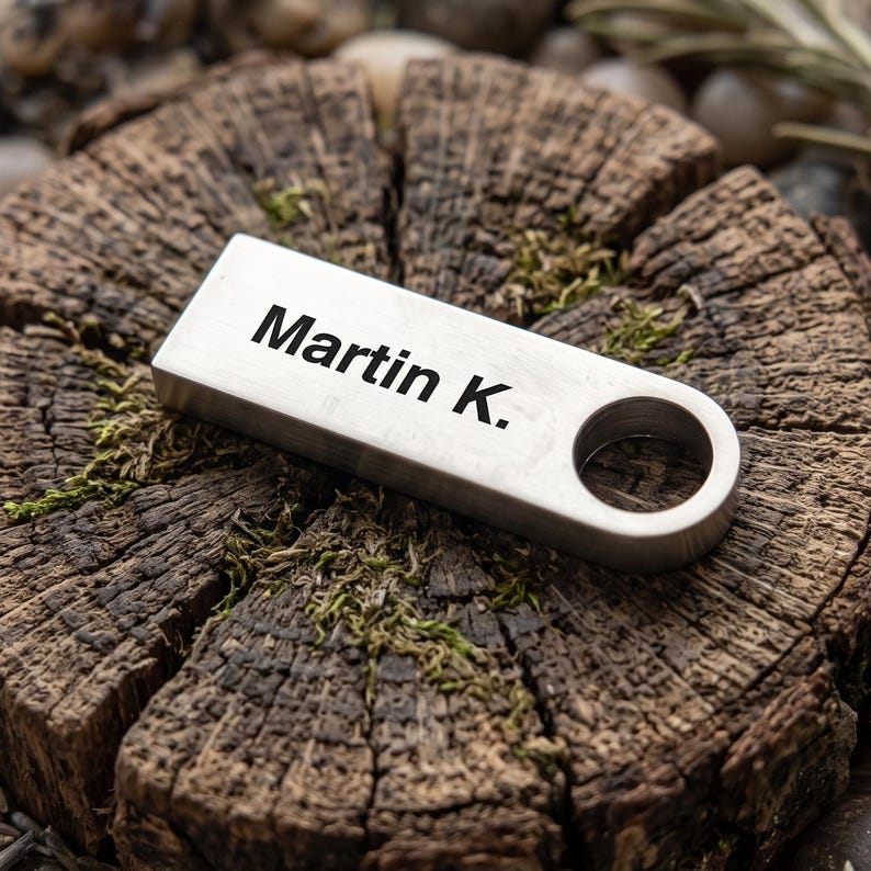 May include: A rectangular silver-toned metal keychain tag with a brushed finish and a circular hole on one end. The surface is engraved with the black text Martin K. in a clean sans-serif font, positioned horizontally across the center of the piece.