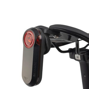 Op de afbeelding: Een zwart en zilver Garmin fietsachterlicht met een rode lens is gemonteerd op een zwart fietsframe. Het licht heeft het Garmin-logo en een zilveren onderkant. Het licht is ontworpen voor veiligheid en zichtbaarheid.