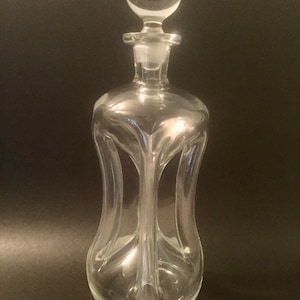 May include: A clear glass decanter with a round stopper. The decanter has a unique, wavy design.