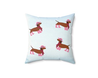 May include: A blue and white pillow with a pattern of four brown dachshunds wearing pink hats and pink polka dot rain boots.