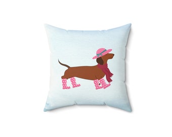Puede incluir: Un dachshund marrón con un sombrero rosa, botas de lluvia de lunares rosas y una bufanda marrón sobre un fondo azul claro.