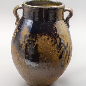 May include: A handcrafted ceramic vase with two handles. The vase features a dark brown and gold glaze with a glossy finish. The vessel has a rounded body and a wide opening, suitable for displaying flowers or as a decorative piece.