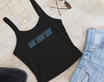May include: Black tank top with the text "GUT LINT OUT" in blue. The top has thin straps and is paired with denim shorts, sunglasses, and a gold necklace. The items are arranged on a light wood-grain surface.
