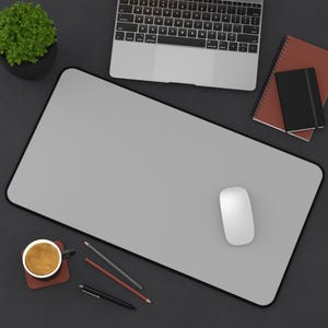 Pu&ograve; includere: Vista dall'alto di uno spazio di lavoro con un tappetino per mouse grigio con bordo nero, un mouse bianco, un laptop, una tazza di caff&egrave; e articoli di cancelleria. Sono presenti anche una piccola pianta in vaso e quaderni.
