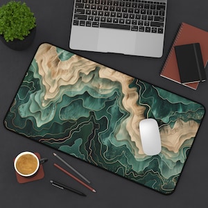 May include: A green and gold abstract design desk mat with a white computer mouse on top. The mat has a textured surface with a wavy pattern.