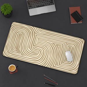 May include: A beige and white striped desk mat with a geometric pattern. The mat is on a black surface with a laptop, a mouse, a cup of coffee, and pencils.