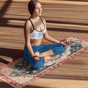 May include: A woman sits in a yoga pose on a colorful patterned yoga mat. She is wearing a blue sports bra with the text "UPLOAD YOUR IMAGE" on it and blue yoga pants. The mat has a red border and intricate floral designs.