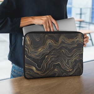 May include: A black laptop sleeve with a gold abstract pattern. The sleeve has a zipper and is made of a soft, durable material.