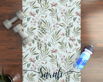 May include: A light blue yoga mat with a floral pattern and the name "Sarah" printed on it. The mat is surrounded by a wooden floor, a water bottle, and a pair of dumbbells.