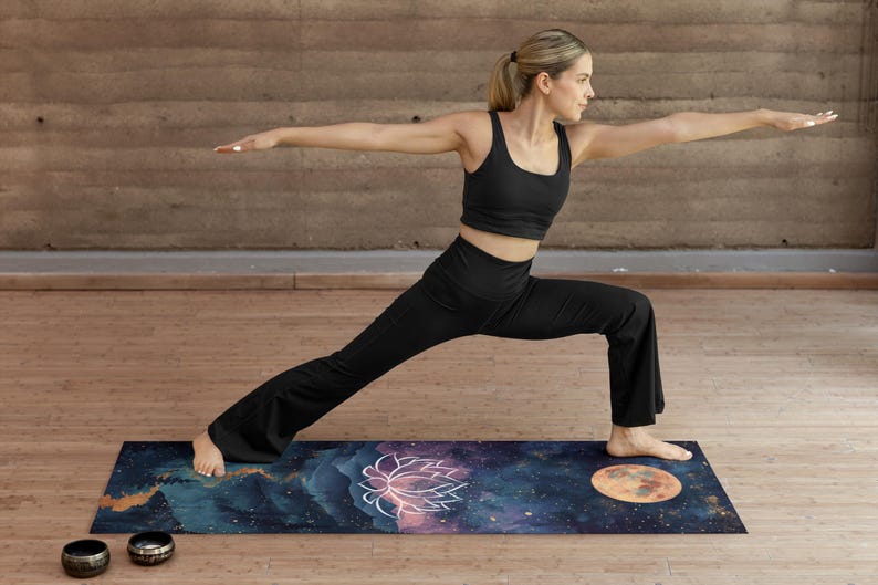 May include: A woman in black yoga pants and a black tank top is doing a yoga pose on a dark blue yoga mat with a galaxy print. The mat has a pink and white lotus flower design and a large orange moon design. Two small metal singing bowls are on the floor next to the mat.