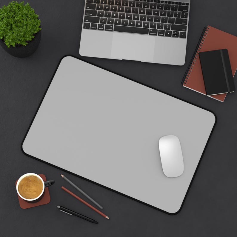 Pu&ograve; includere: Vista dall'alto di uno spazio di lavoro con un tappetino per mouse grigio con bordo nero, un mouse bianco, un laptop, una tazza di caff&egrave; e cancelleria. &Egrave; visibile anche una piccola pianta in vaso.