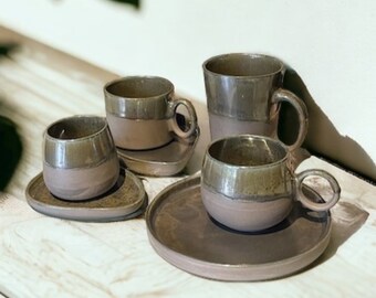 May include: Set of four ceramic coffee cups and saucers in shades of brown and green. The cups have a rounded shape and a slightly flared lip. The saucers are round and have a slightly raised edge.