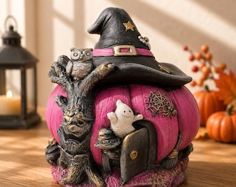Könnte beinhalten: Eine dekorative Figur in Form eines rosa Kürbishauses mit einem schwarzen Hexenhut als Dach. Das Haus zeigt einen strukturierten Baumstamm, eine kleine graue Eule, eine weiße Geisterfigur, ein Spinnennetz und eine kleine Tür.