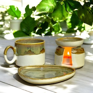 May include: A ceramic teacup and saucer set with a green and brown glaze. The saucer is oval shaped. A ceramic oil burner with a candle inside is also included. The oil burner has a green and brown glaze.