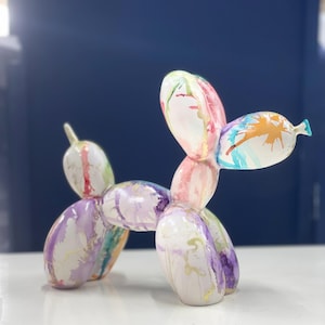 Peut inclure: Une sculpture d'animal en ballon blanc en forme de chien avec des éclaboussures de peinture colorées. Le chien est debout sur une surface blanche.