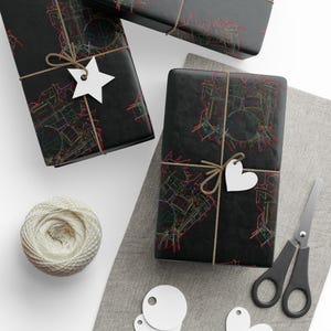 May include: Three wrapped gifts with black paper featuring a colorful drum set design. Each package is tied with twine and has a white tag. A ball of twine, scissors, and additional tags are also visible.