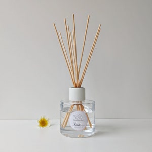 May include: A clear glass diffuser bottle with a white lid and wooden sticks. The bottle has a label that says "Coo Candles" and "Rose".