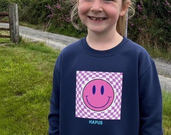Welsh 'hapus' emoji smiley face checkered pink girl pattern jumper. Smiley faces cool trending pink and purple jumper. Siwmper gwyneb hapus