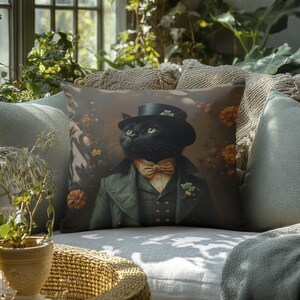 May include: A black cat wearing a green suit and a top hat sits on a throw pillow with a floral pattern. The pillow is on a light gray couch with a green throw blanket. The couch is in a room with a window and plants.