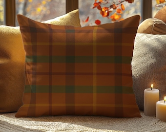 May include: A square decorative pillow with a plaid pattern in shades of orange, brown, and green. The pillow is placed among other pillows and lit candles, creating a cozy and inviting atmosphere. The pillow is likely used for home decor.