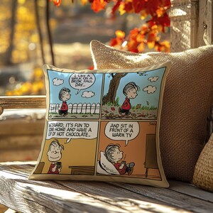 Może przedstawiać: Kwadratowa poduszka z komiksem z Linusem z Peanuts. Komiks pokazuje Linusa cieszącego się jesiennym dniem, pijącego gorącą czekoladę i oglądającego telewizję. Poduszka ma beżową obw&oacute;dkę i leży na drewnianej powierzchni.