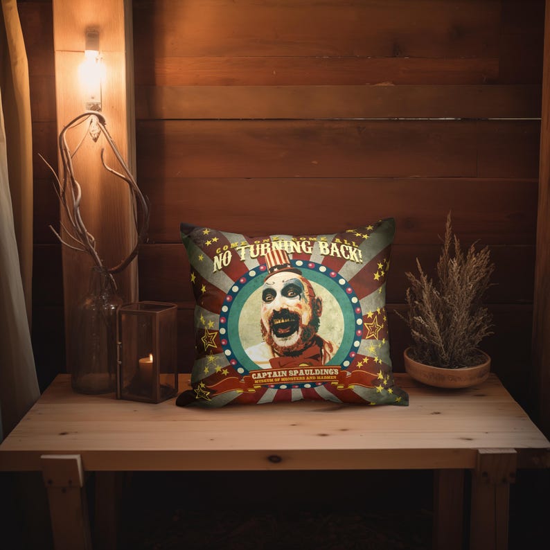 May include: A red, white, and blue pillow with a vintage circus theme. The pillow features a portrait of Captain Spaulding, a character from the horror film series "House of 1000 Corpses". The text on the pillow reads "Come One Come All! No Turning Back!"