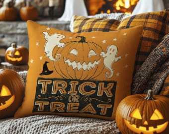 May include: Orange Halloween-themed pillow with a jack-o'-lantern design, two white ghosts, and the words "TRICK OR TREAT" in black. The pillow is surrounded by pumpkins and a cozy blanket, perfect for fall decor.