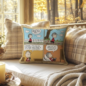 Może przedstawiać: Beżowa kwadratowa poduszka z komiksem przedstawiającym chłopca w czerwonej koszuli. Komiks pokazuje chłopca spacerującego, pijącego gorącą czekoladę i oglądającego telewizję. Tekst zawiera "Lubię spacer w chłodny jesienny dzień" i "I usiąść przed ciepłym telewizorem".