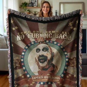 May include: A woven throw blanket with a red, white, and blue color scheme. It features a caricature of Captain Spaulding from the movie "House of 1000 Corpses" with the text "Come one, come all, no turning back!" and "Captain Spaulding's Museum of Monsters and Madmen".