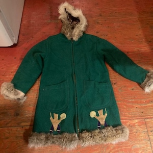 May include: A green hooded winter coat with a fur trim. The coat has two pockets and two embroidered figures on the front.