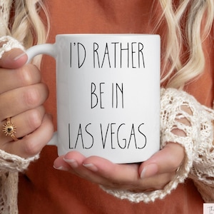 May include: White ceramic mug with black text that reads "I'd rather be in Las Vegas".