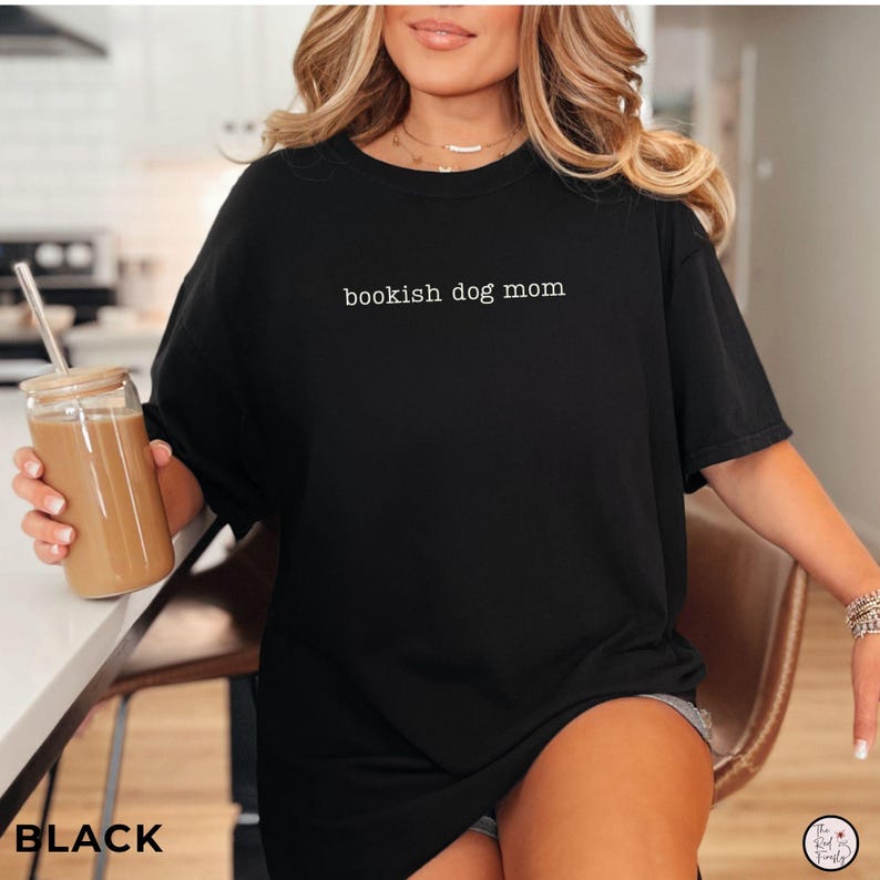 May include: A black short-sleeved t-shirt featuring the white text "bookish dog mom" printed in a simple, lowercase font across the center of the chest. The garment has a crew neckline and a relaxed fit, providing a casual look for daily wear.