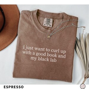 K&ouml;nnte beinhalten: Espressofarbenes T-Shirt mit dem wei&szlig;en Text "i just want to curl up with a good book and my black lab". Das Shirt hat einen Rundhalsausschnitt und kurze &Auml;rmel. Eine silberne Halskette mit Anh&auml;nger liegt auf dem Shirt.