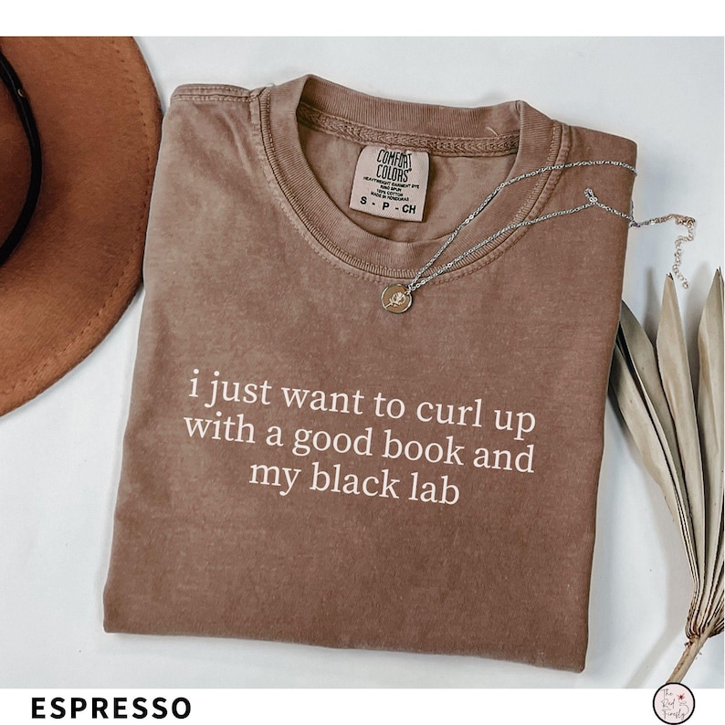 K&ouml;nnte beinhalten: Espressofarbenes T-Shirt mit dem wei&szlig;en Text "i just want to curl up with a good book and my black lab". Das Shirt hat einen Rundhalsausschnitt und kurze &Auml;rmel. Eine silberne Halskette mit Anh&auml;nger liegt auf dem Shirt.